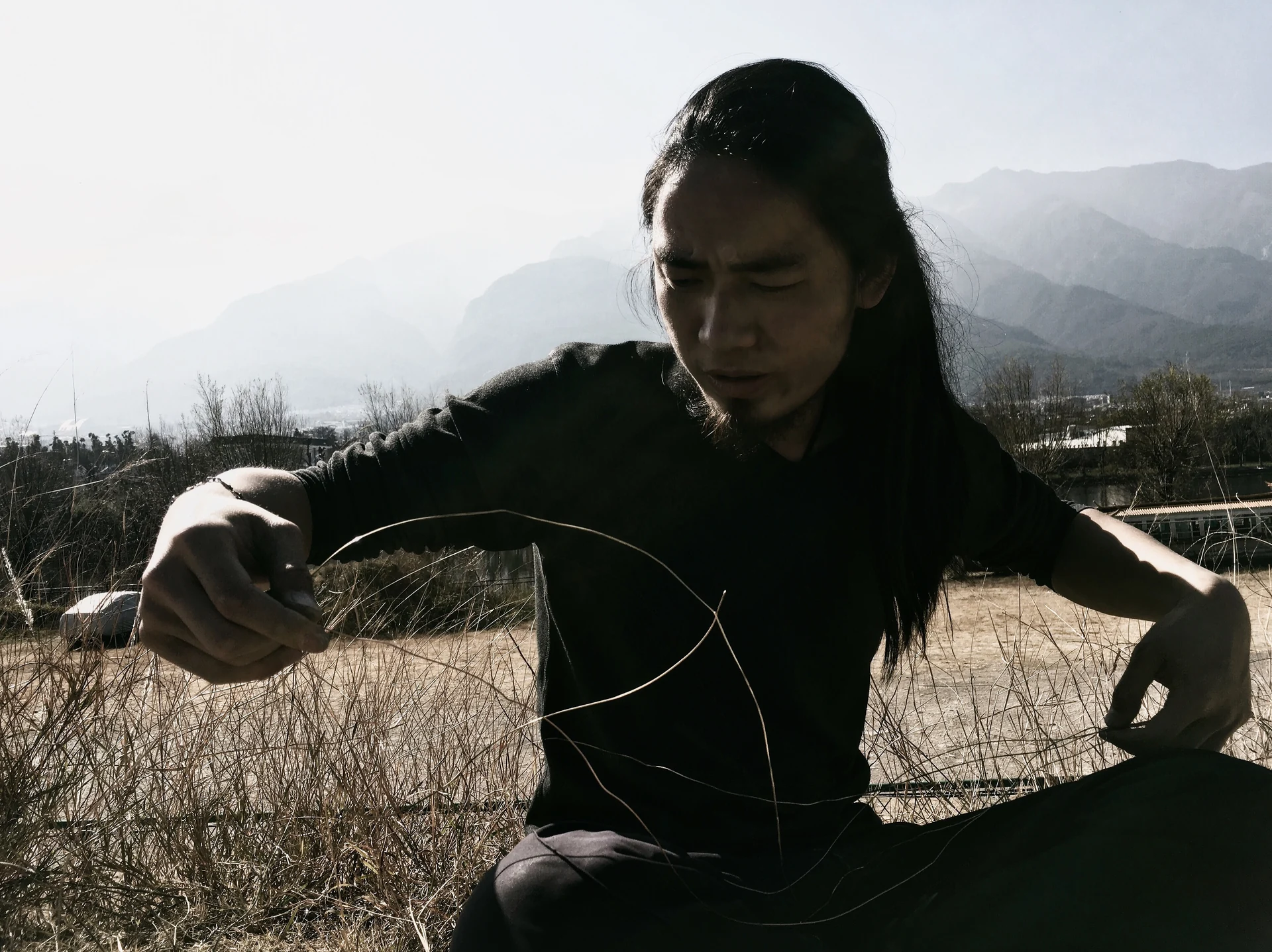 A craftsperson shaping wire outdoors in a mountain landscape